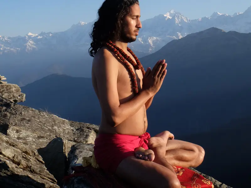 A man meditating on a mountain ledge in the Himalayas